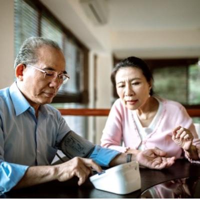 A man checking his blood pressure at home with his wife helping. 