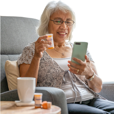 a lady in a lazyboy at home cross referencing her prescription drug bottle with information on her mobile phone.