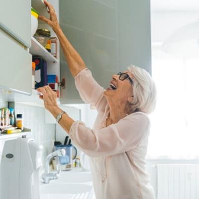A senior women reaching into a high cabinet above her kitchen sink