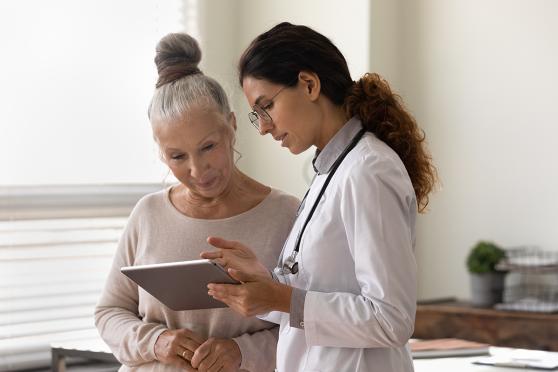Senior woman talking to doctor and looking at chart on digital device